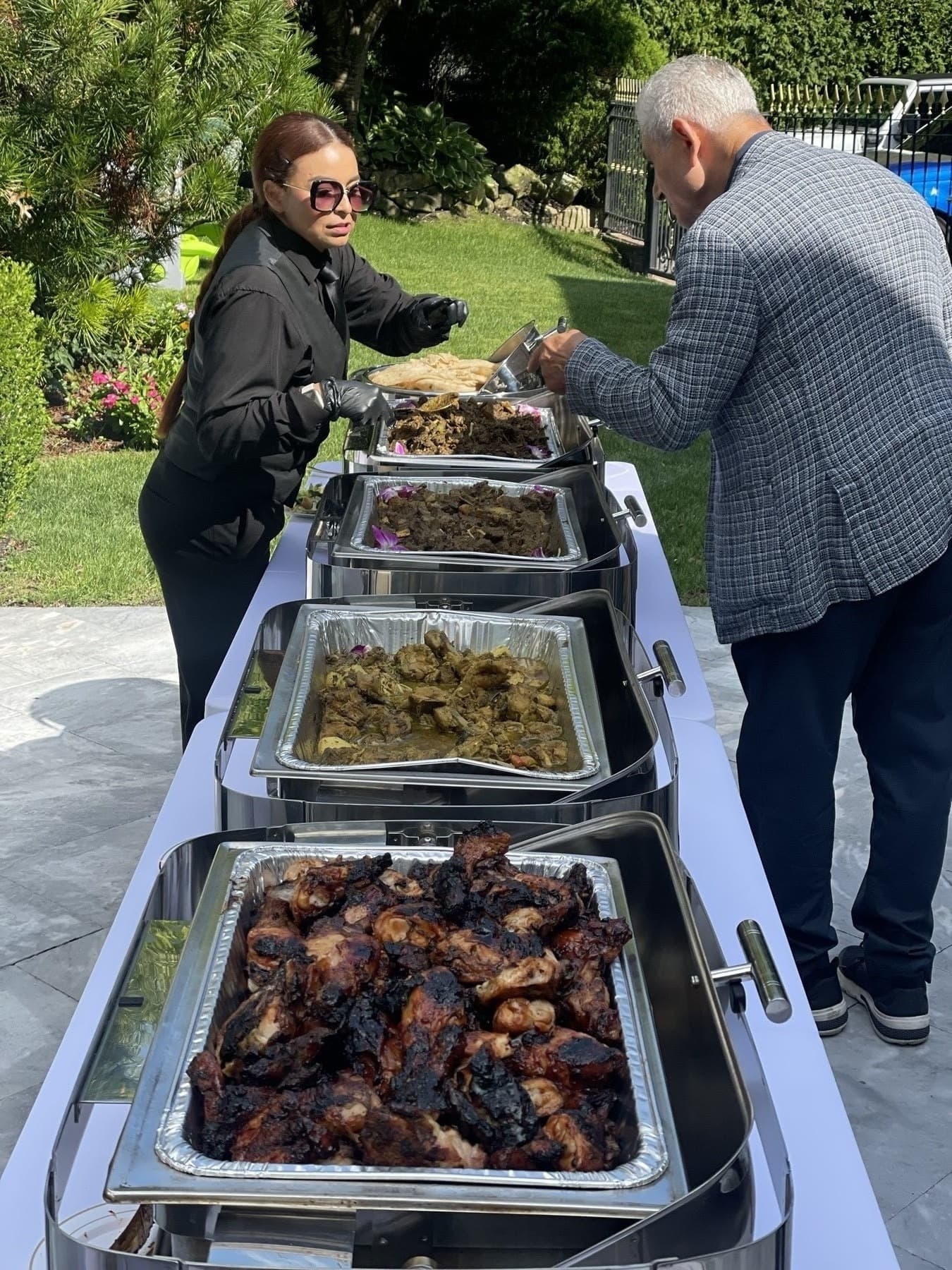 Chef Michael Saroop serving guests from a line of chafing dishes at an outdoor event